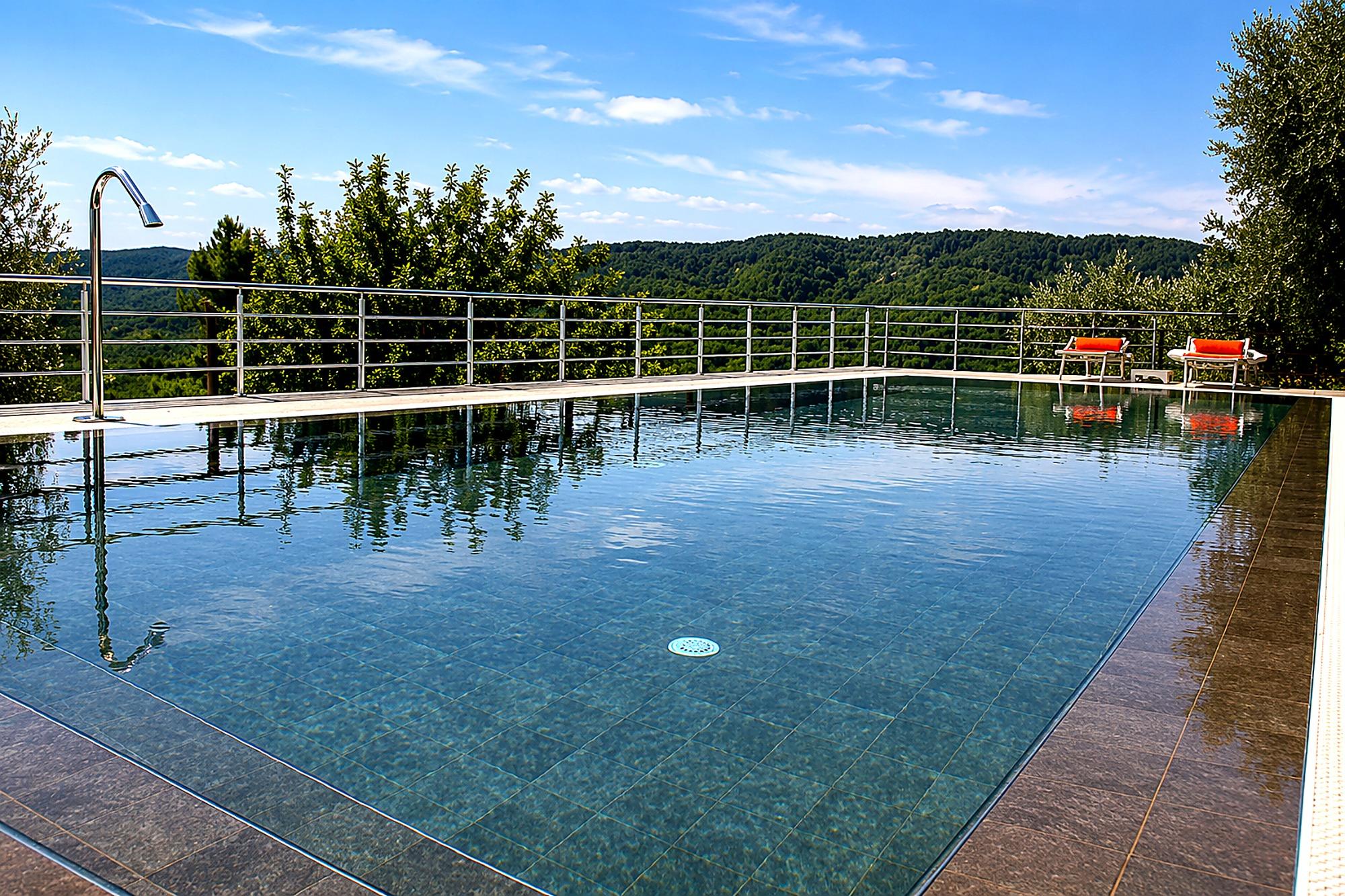 Piscina con fondo scuro immersa nel verde, con vista sul Gargano