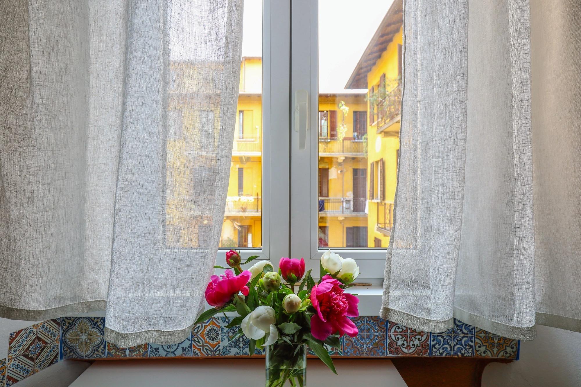 Peonie alla finestra di House of Frames Milano, con vista su un tipico cortile milanese.
