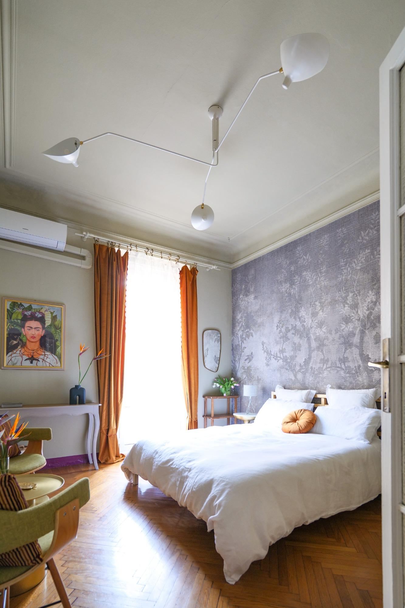 Camera matrimoniale luminosa di design a Milano con parquet, carta da parati scenografica e dettagli iconici di interior design.