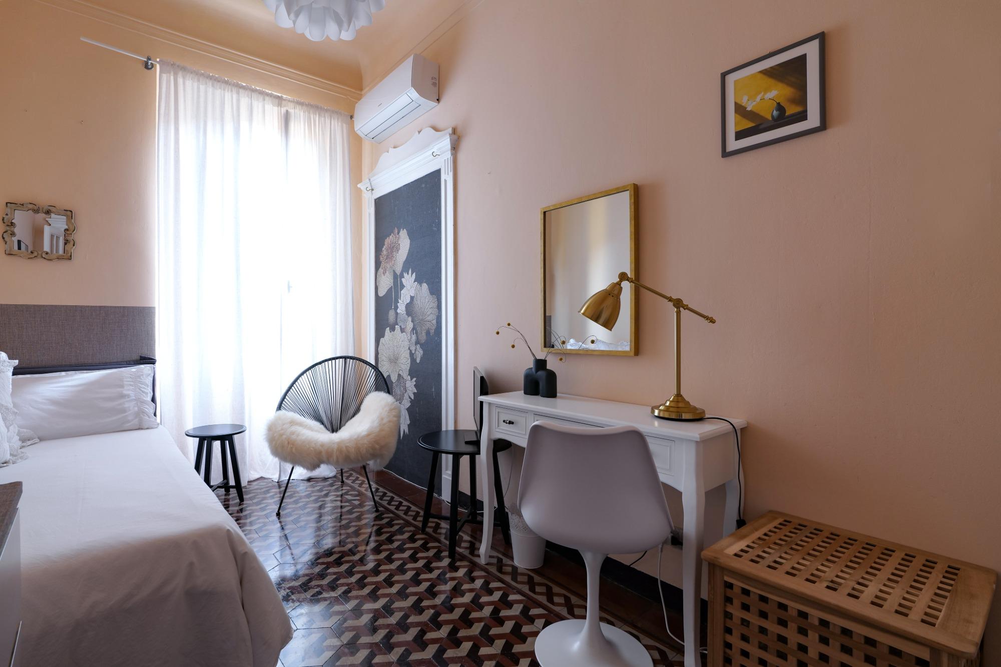 Camera singola di House of Frames Milano con poltrona Acapulco, scrittoio bianco e pavimento originale in cementine