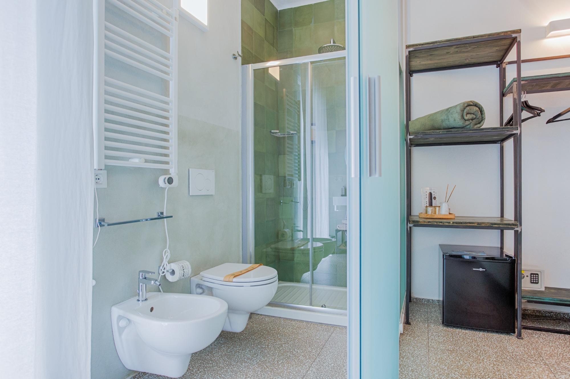 Moderno bagno privato della Camera Verde con rivestimento doccia verde oliva, sanitari sospesi e phon a muro.