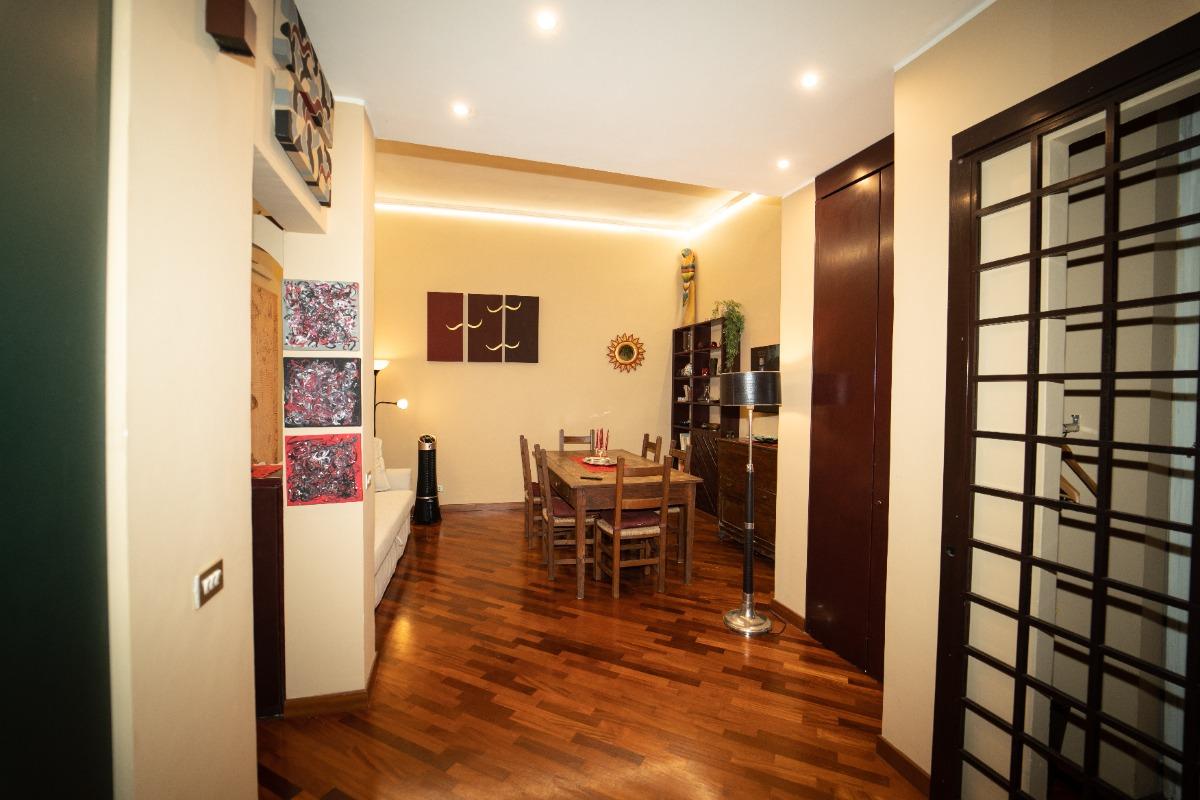 Panoramica dell'ingresso e del soggiorno. Grande tavolo in legno e un comodo divano letto. Un grande armadio. Elegante ed elegante lampada a colonna.