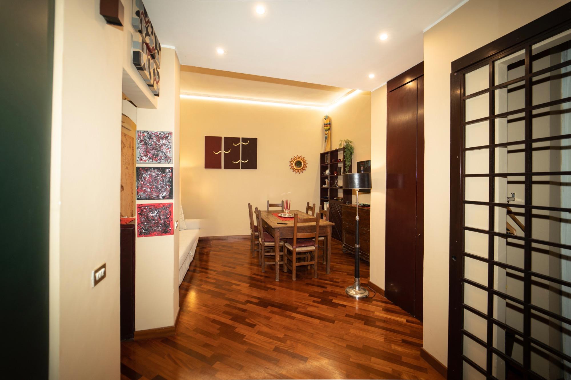 Panoramica dell'ingresso e del soggiorno. Grande tavolo in legno e un comodo divano letto. Un grande armadio. Elegante ed elegante lampada a colonna.