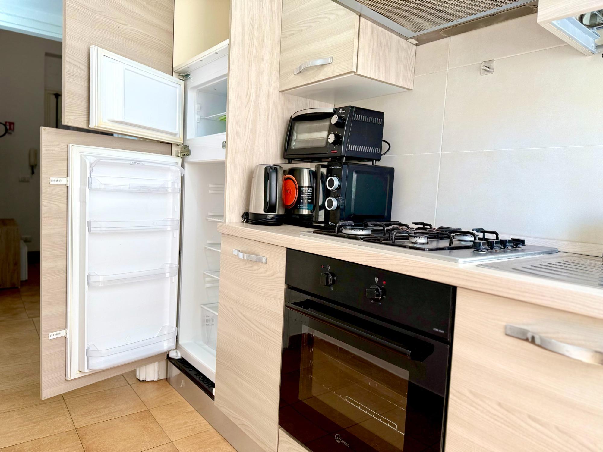 Una cucina moderna e completamente attrezzata con mobili in legno chiaro, dotata di tostapane, microonde, bollitore elettrico, frigorifero con congela