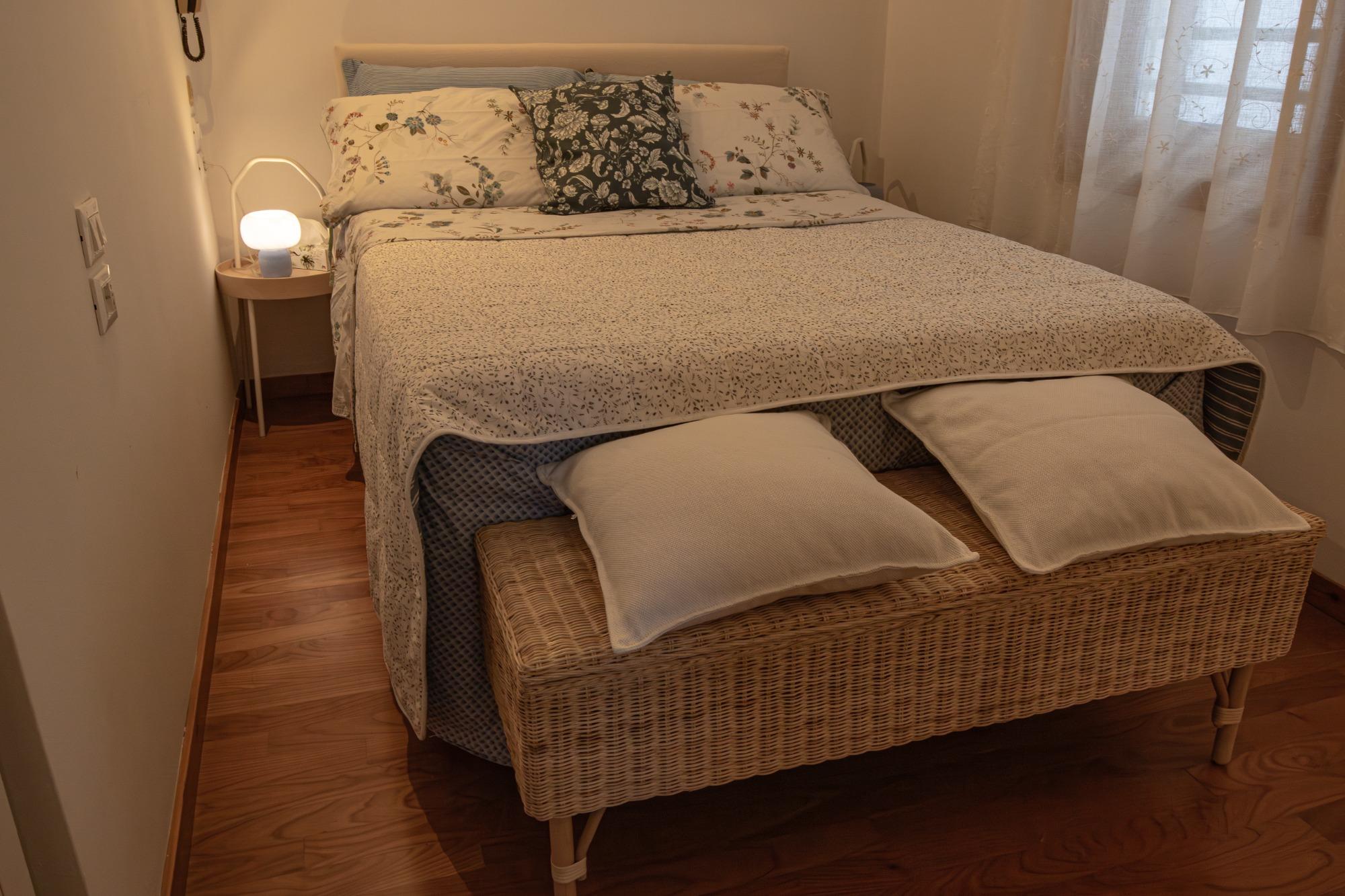 Camerda da letto con due comodini, panchetta in vimini e letto ad una piazza e mezza francese