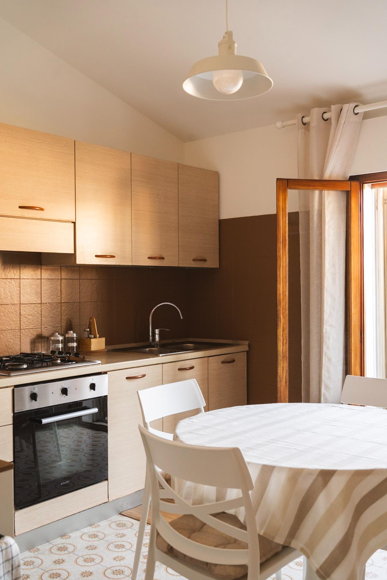 Cucina con piano cottura, frigo standard, posateria, piatti, bicchieri, forno