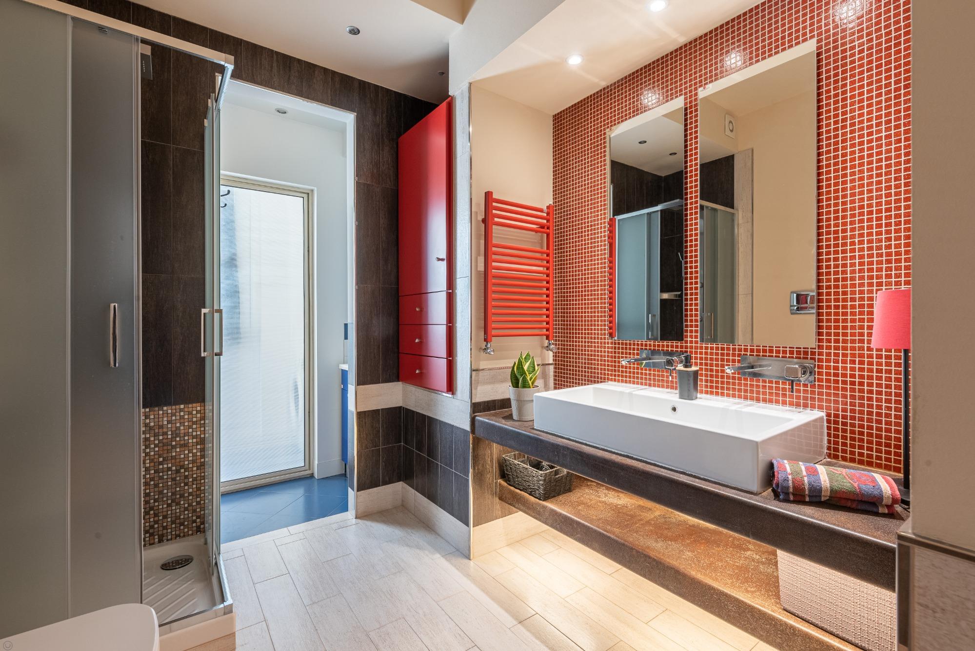 Dettagli di stile: il mosaico rosso si sposa perfettamente con il termoarredo e i mobili su misura. Un bagno di design, colorato e raffinato, per il t