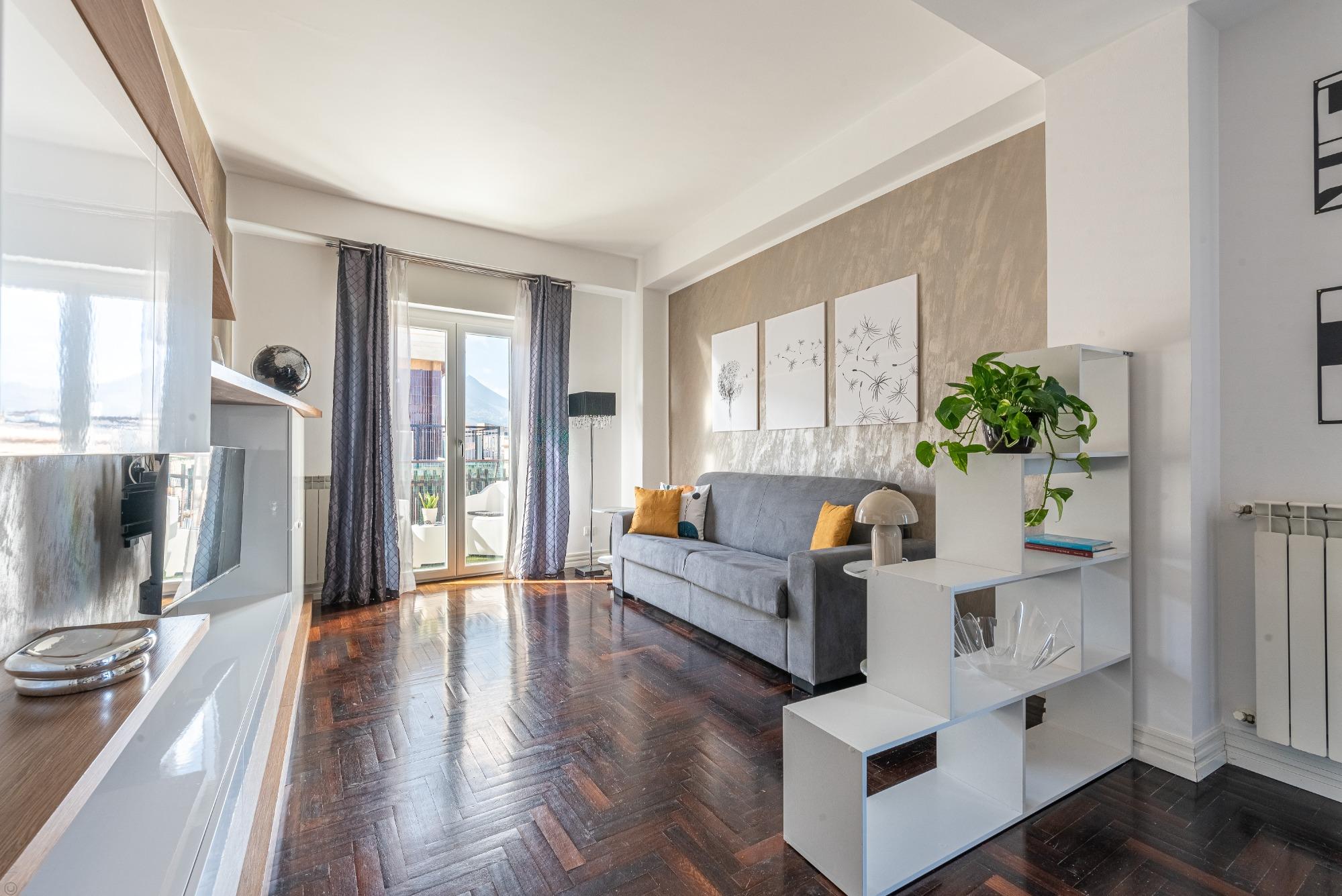 Zona living accogliente: divano, parete attrezzata con Smart TV 40" e libreria bianca che separa l'area pranzo. Design e comfort per il tuo soggiorno.